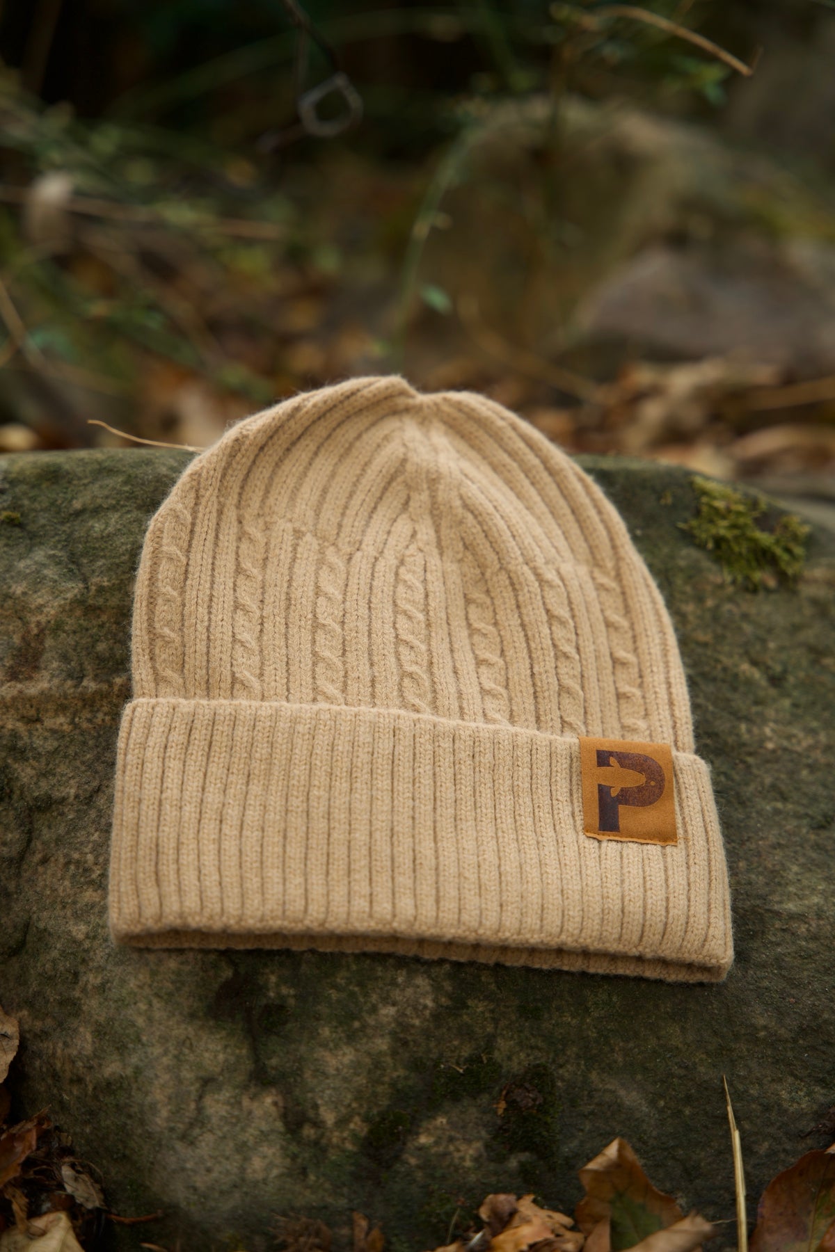 P Mütze in Beige mit Zopfmuster auf einem bemoosten Stein